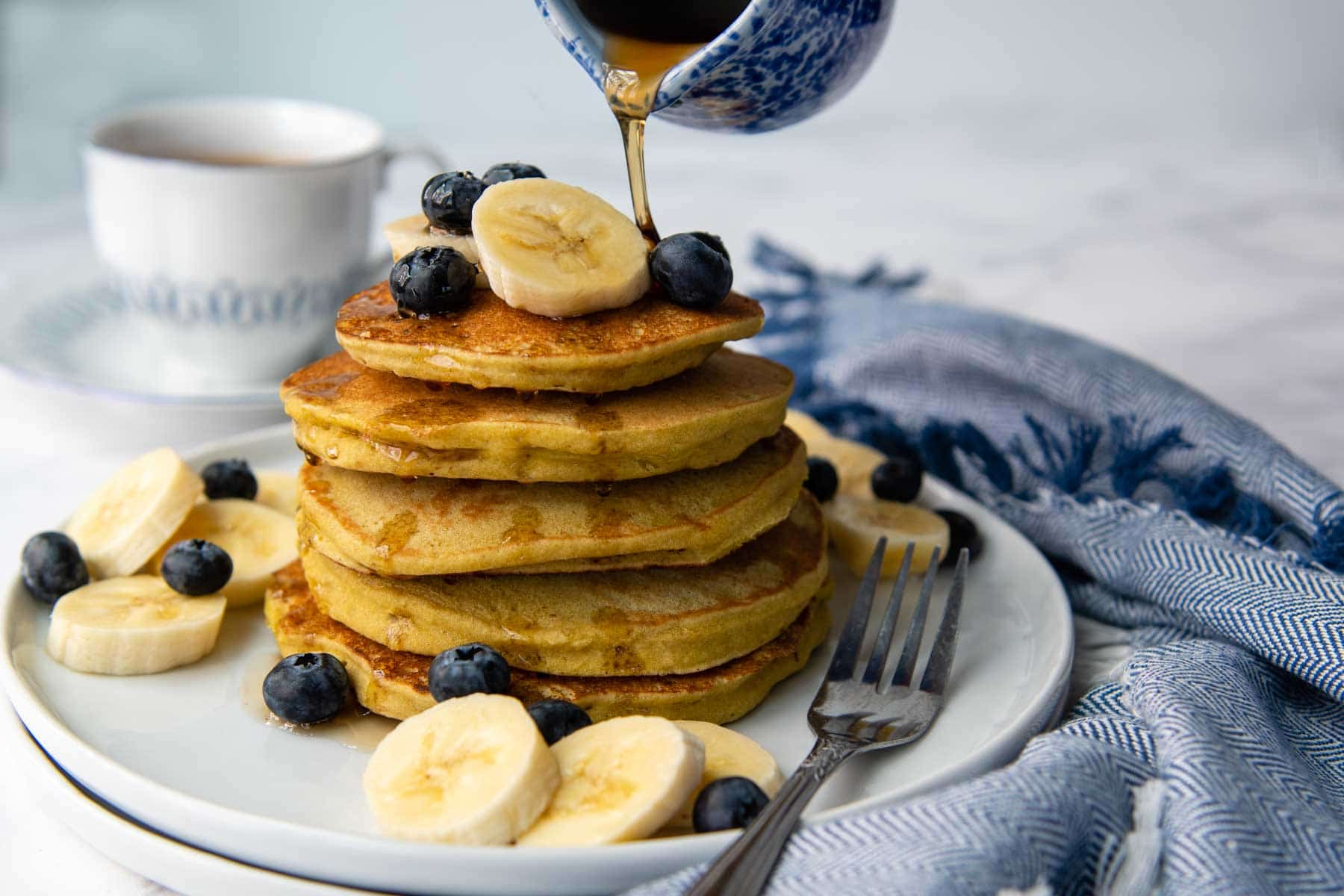 a small blue carafe pouring syrup on top of the pancakes.