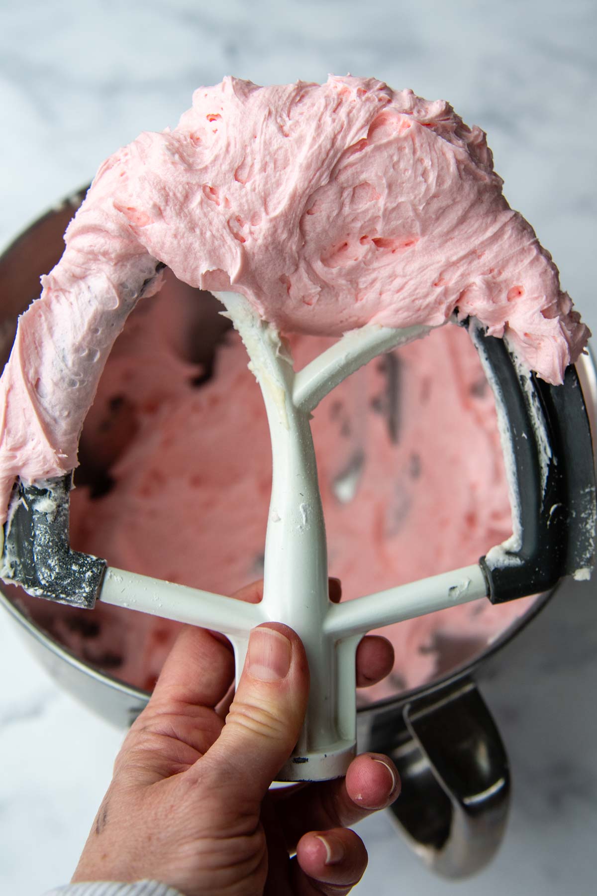 a beater holding up fluffy pink frosting.