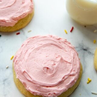 a pink sugar cookie on a white background with sprinkles around and a glass of milk.