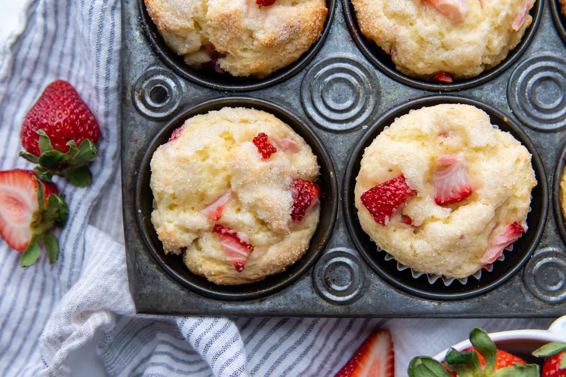 An overhead shot of two muffins in a vintage muffin pan with fresh strawberries next to it.