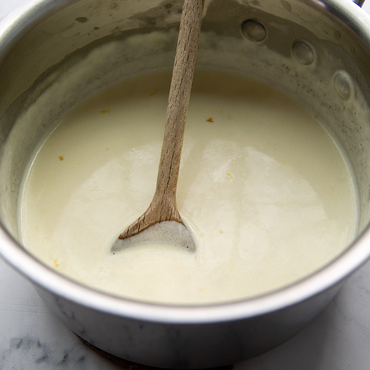 a sauce pan with the creamy lemon sauce and a wooden spoon.
