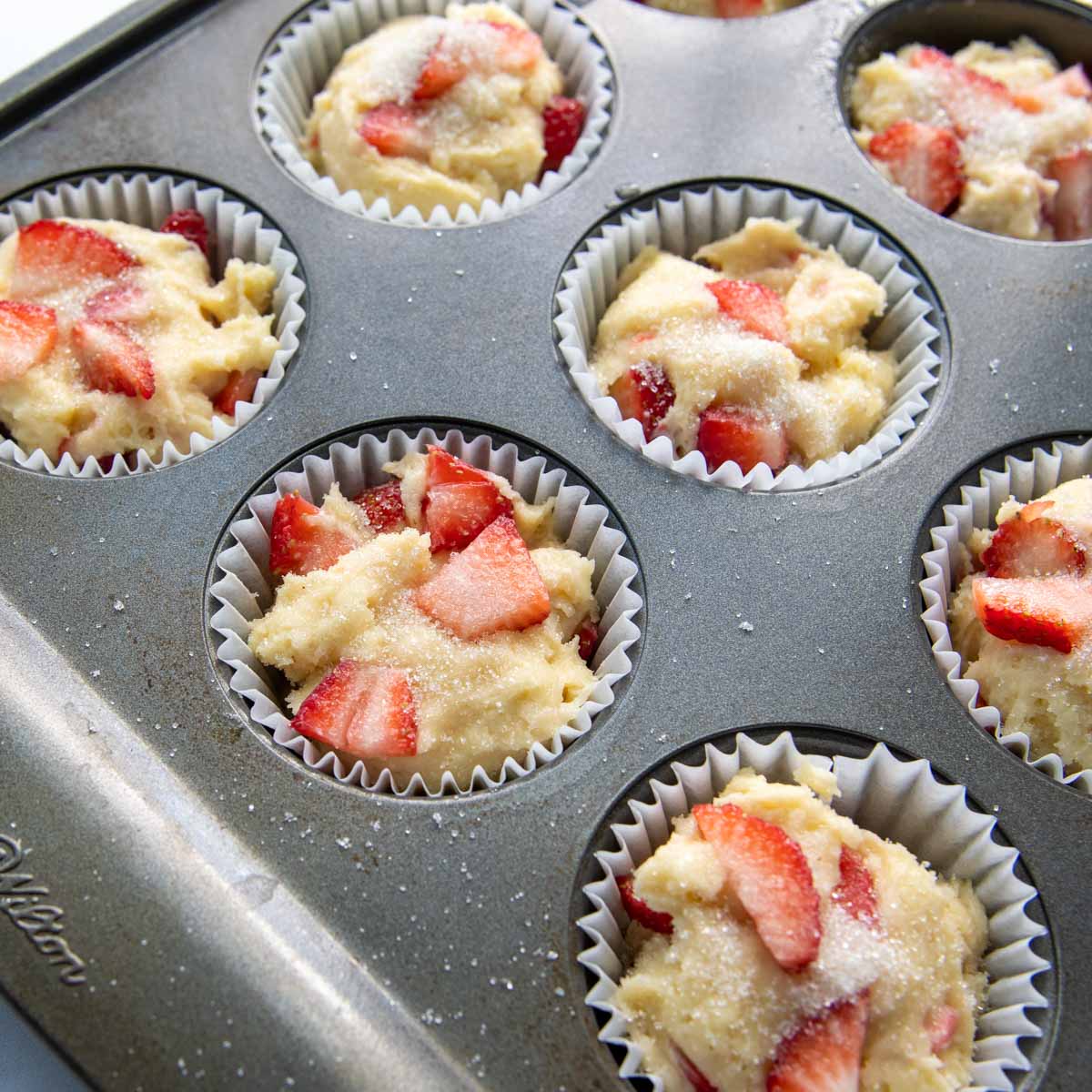 unbaked muffins in a muffin pan with sugar sprinkled on the tops.