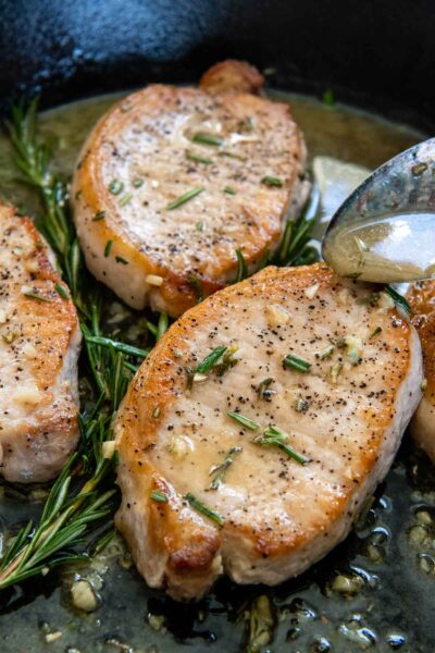 a spoon drizzling sauce over the top of pork chops.