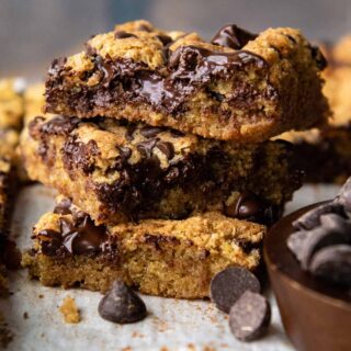 a stack of 3 blondies with melted chocolate and chocolate chips scattered around