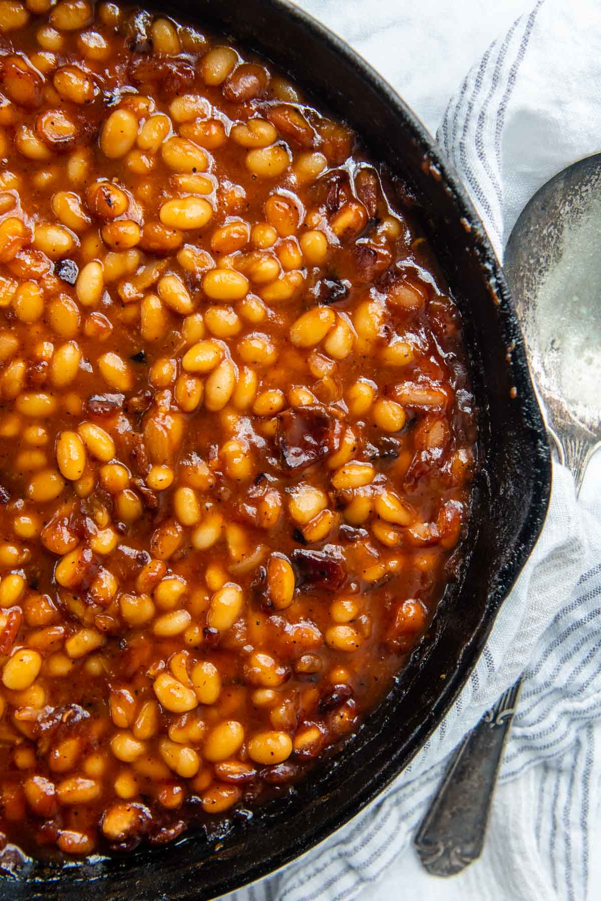 overhead shot of baked beans in a cast iron skillet with a spoon next to it.