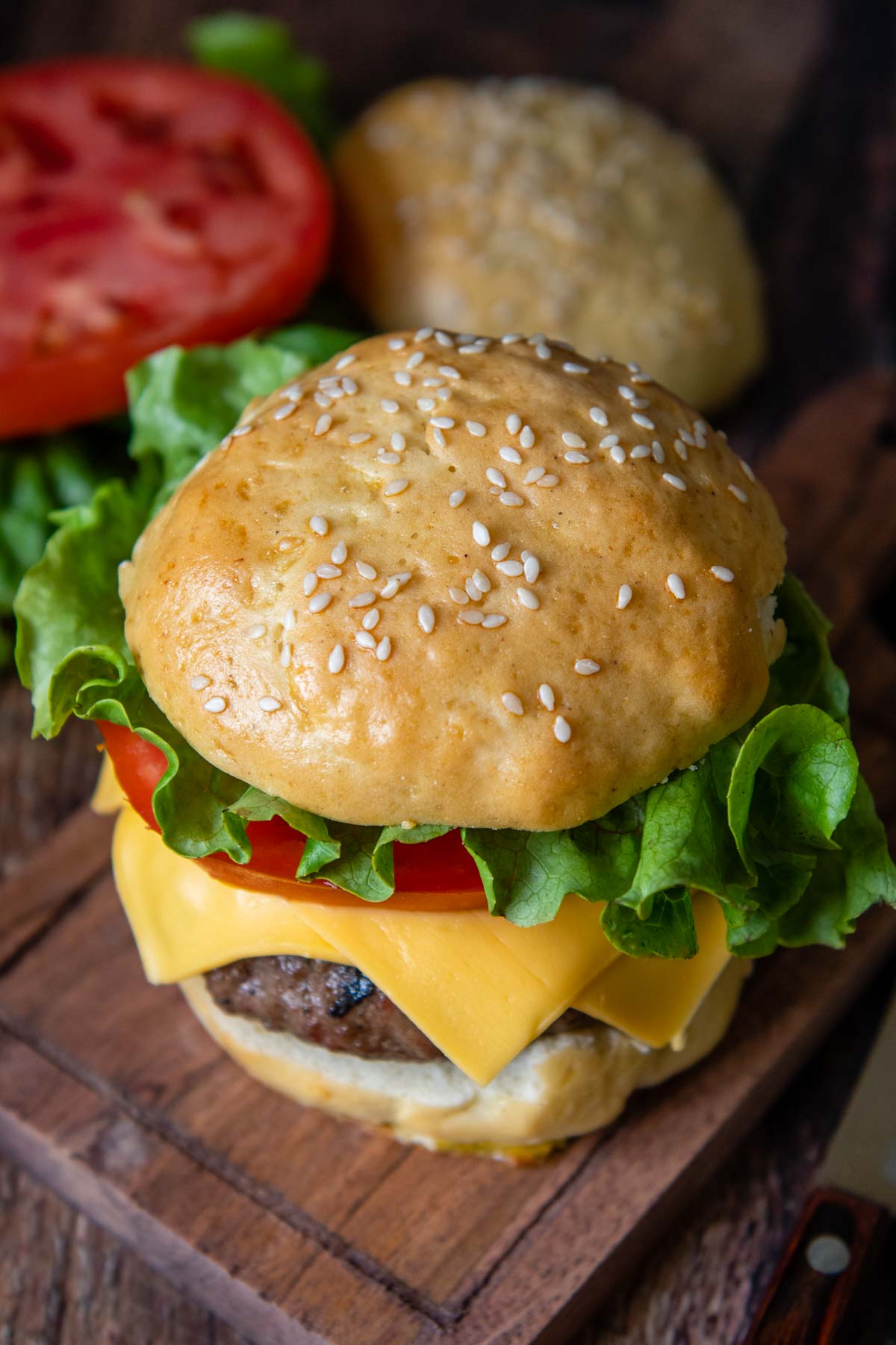 a burger with lettuce, tomato, and cheese on a wood cutting board.