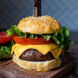 a straight on shot of an assembled burger with a knife stabbed into the top.