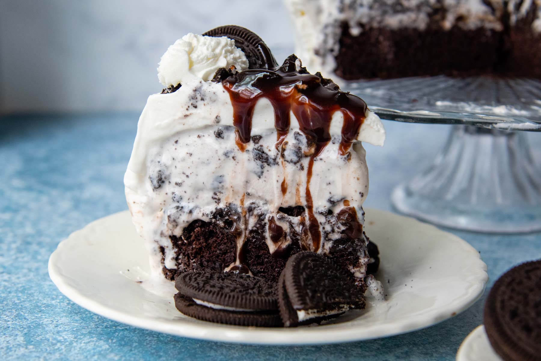 a slice of ice cream cake on a white plate with hot fudge dripping down on top.