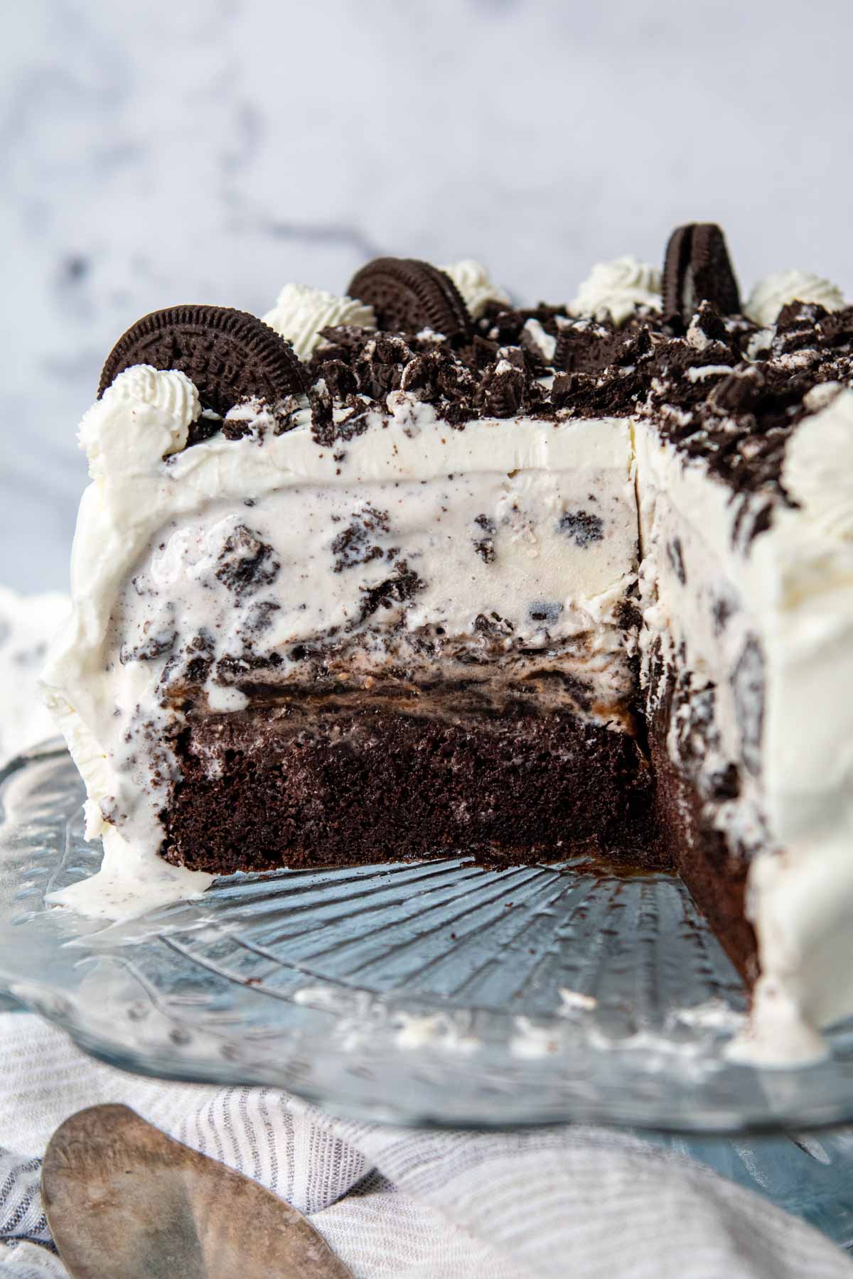 an oreo ice cream cake on a cake stand with a slice out.