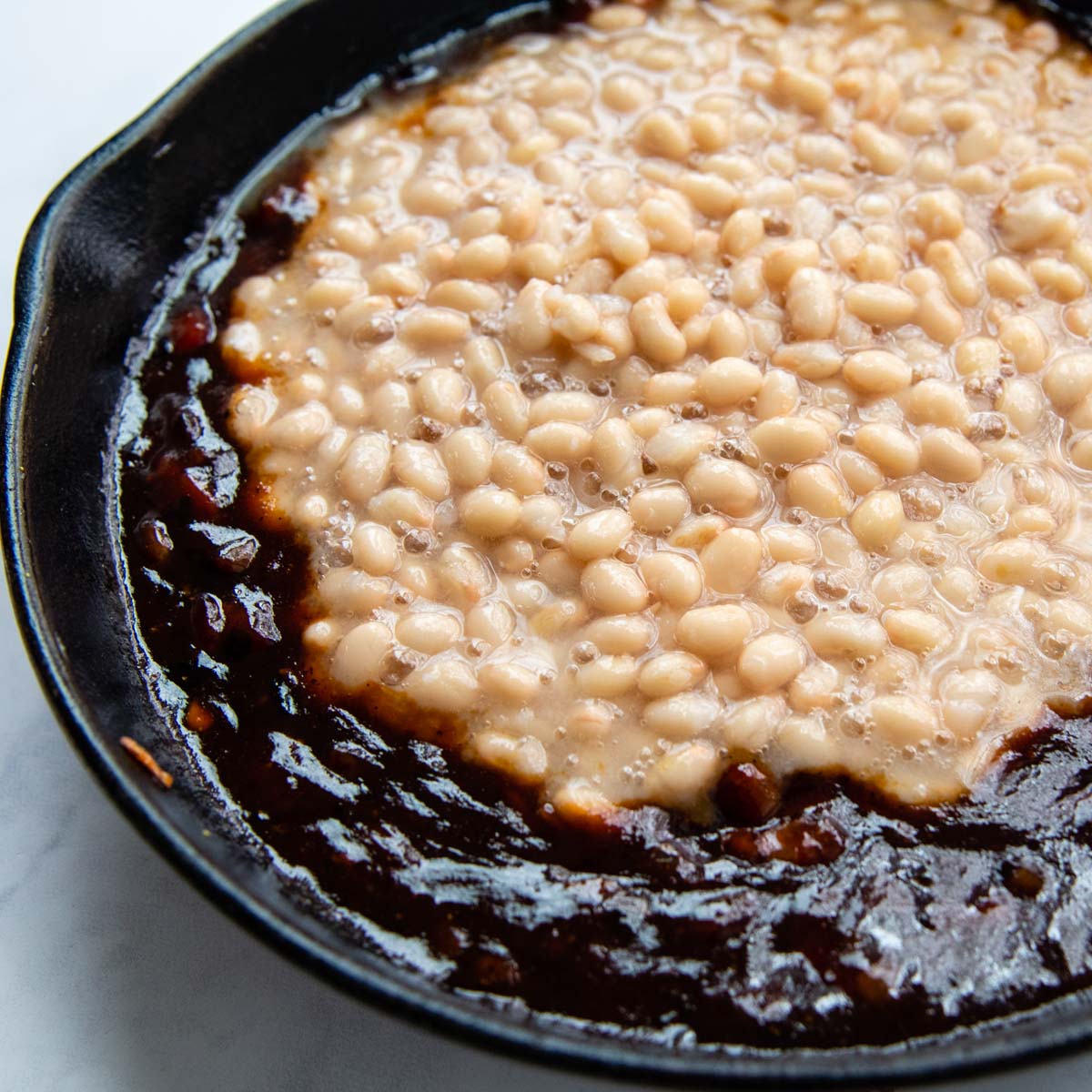 image showing the beans being stirred into the sauce.