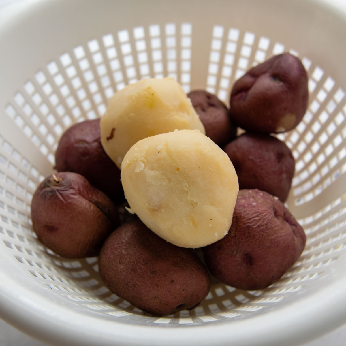boiled potatoes in a colander with one peeled.