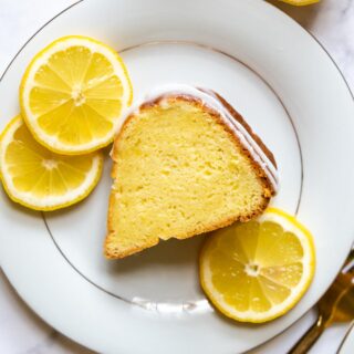 a slice of lemon cake on a white plate with lemon slices next to it.