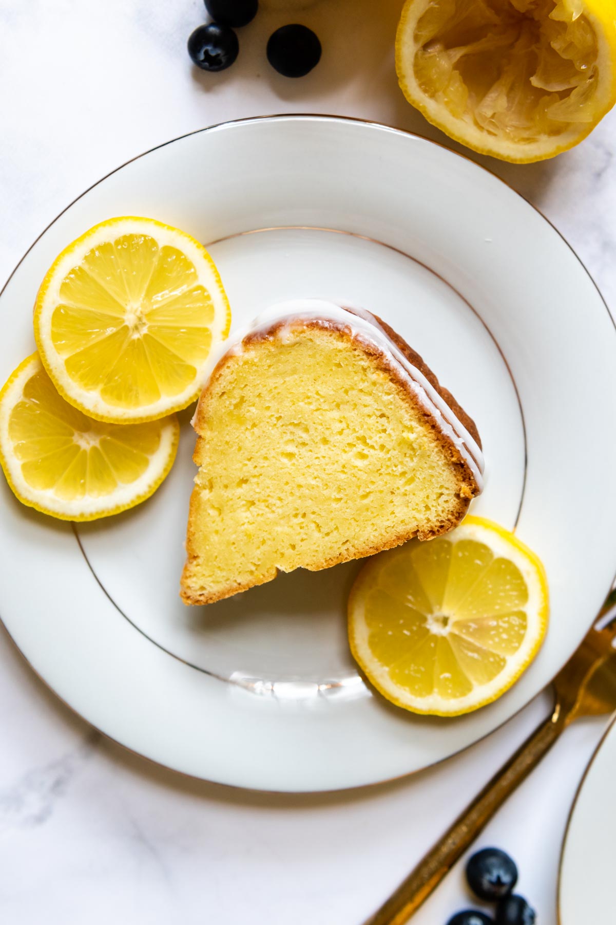 a slice of lemon cake on a white plate with lemon slices next to it.