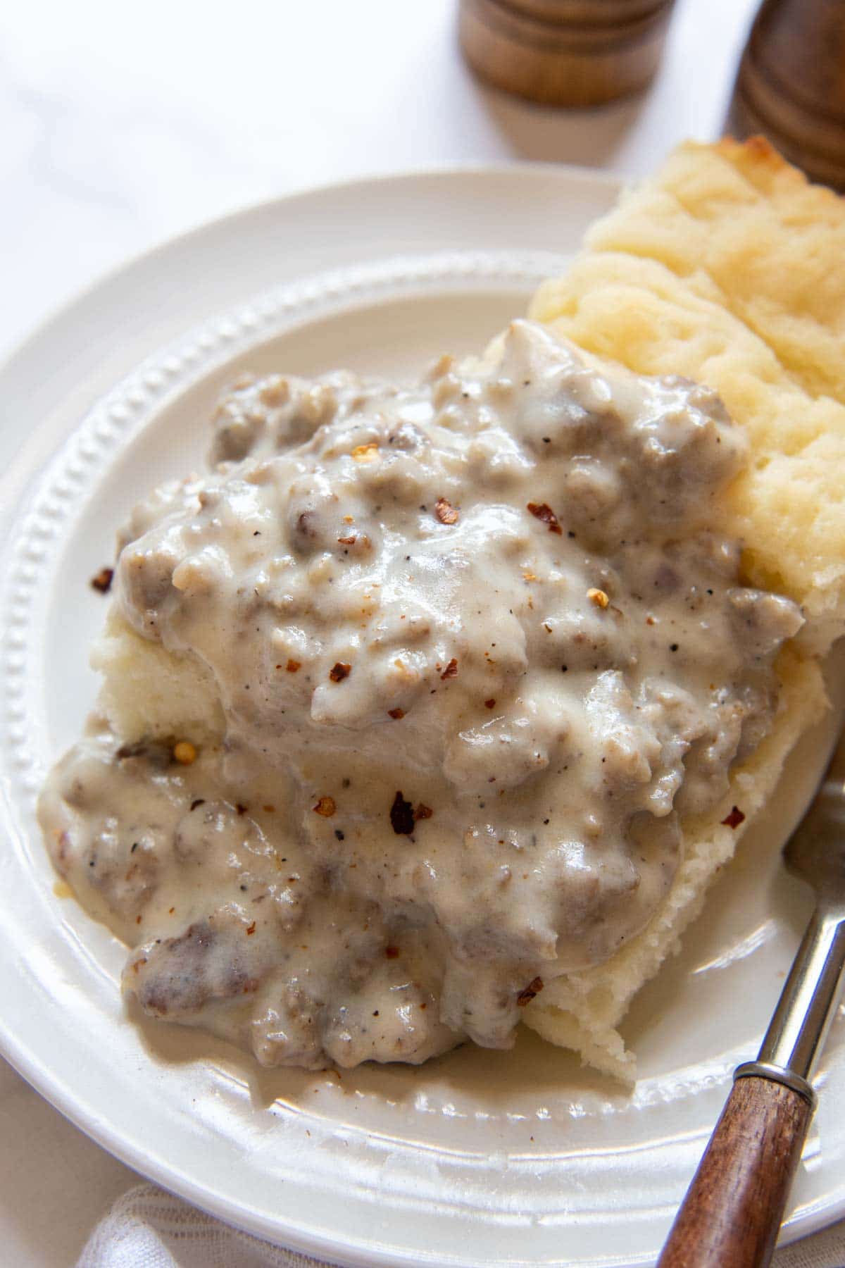 sausage gravy over gluten free biscuits on a white plate.