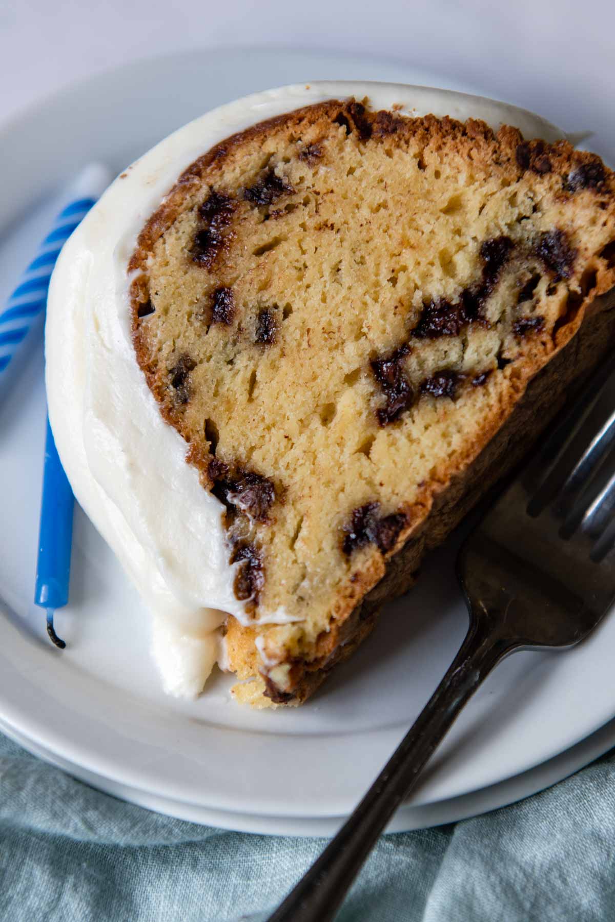a slice of chocolate chip cake on a white plate with a fork resting next to it.