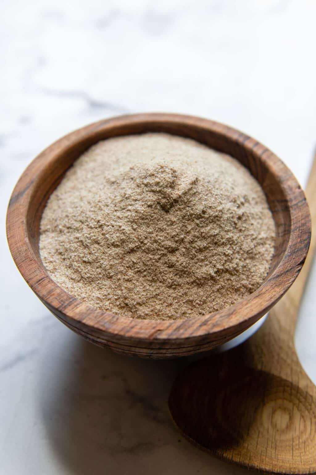 a wooden bowl of psyllium husk powder with spoon laying next to it