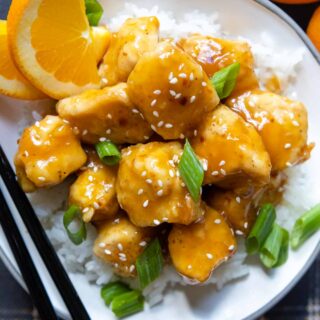 overhead shot of a serving of gluten free orange chicken in a white bowl with chopsticks.