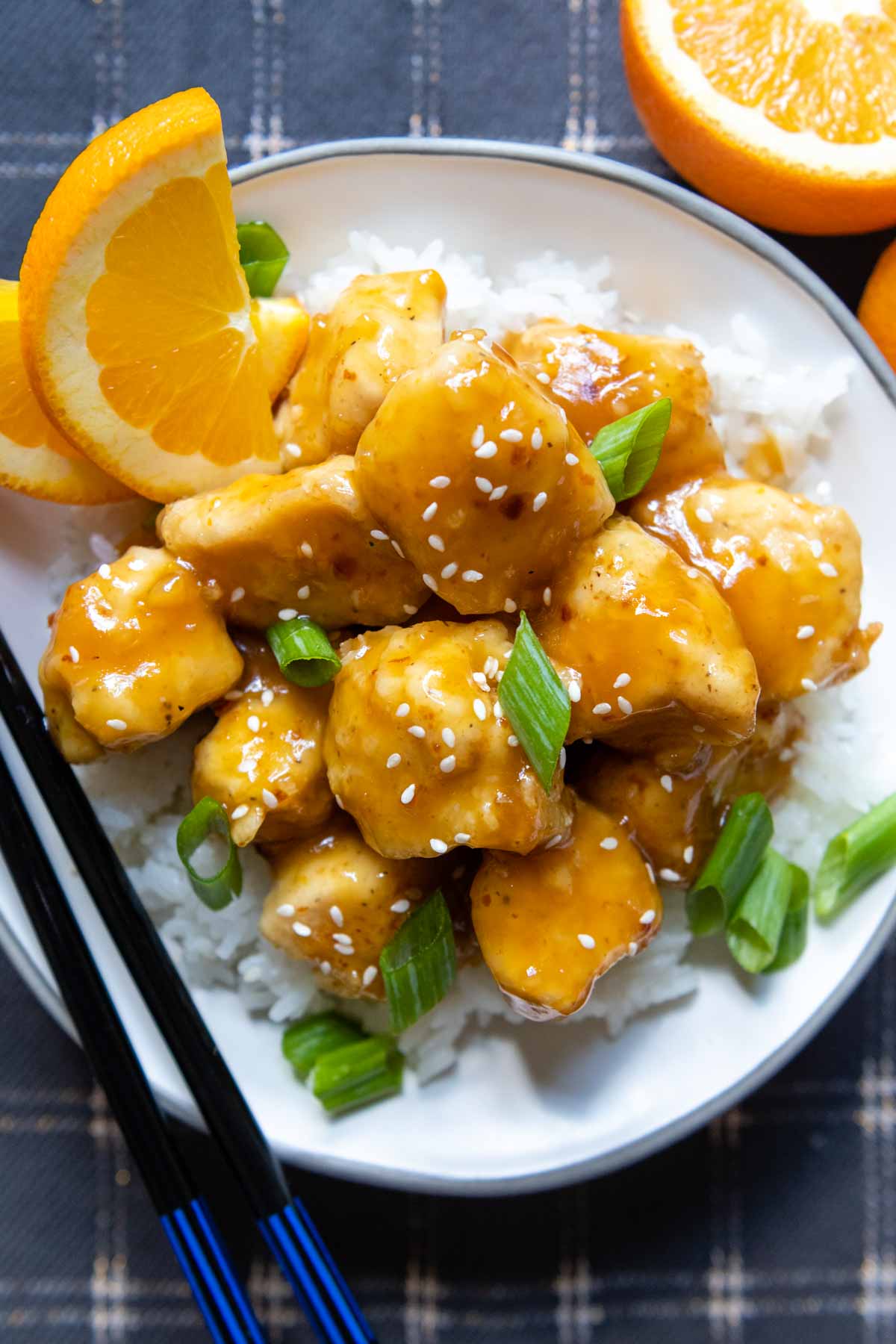 overhead shot of a serving of gluten free orange chicken in a white bowl with chopsticks.