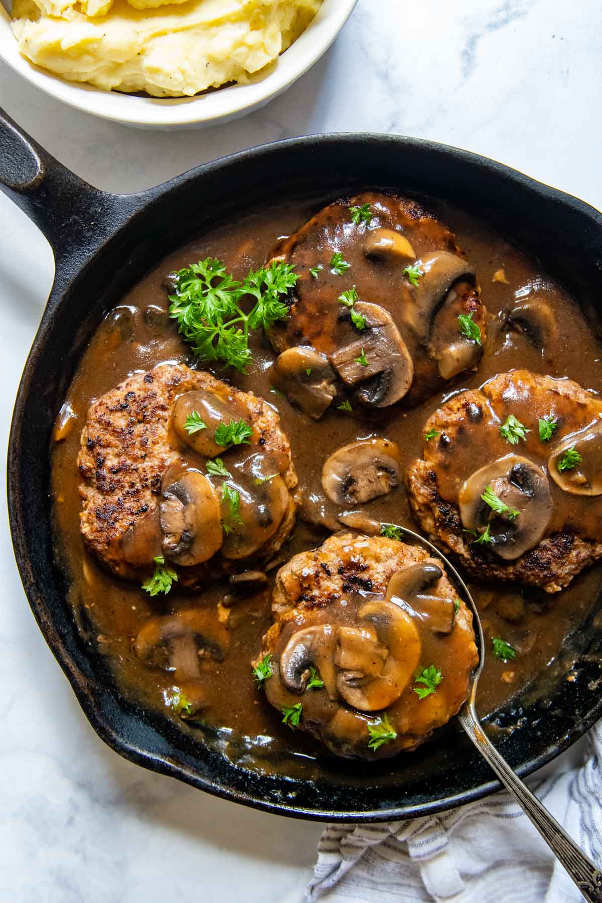 cooked salisbury steaks with gravy in a cast iron skillet.