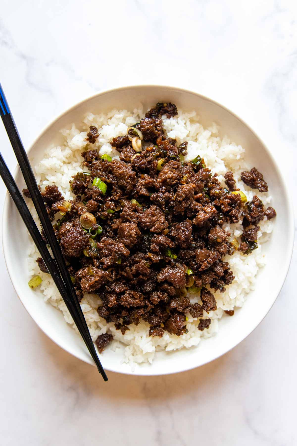 overhead show to bulgogi served over rice with chopsticks on a white background.