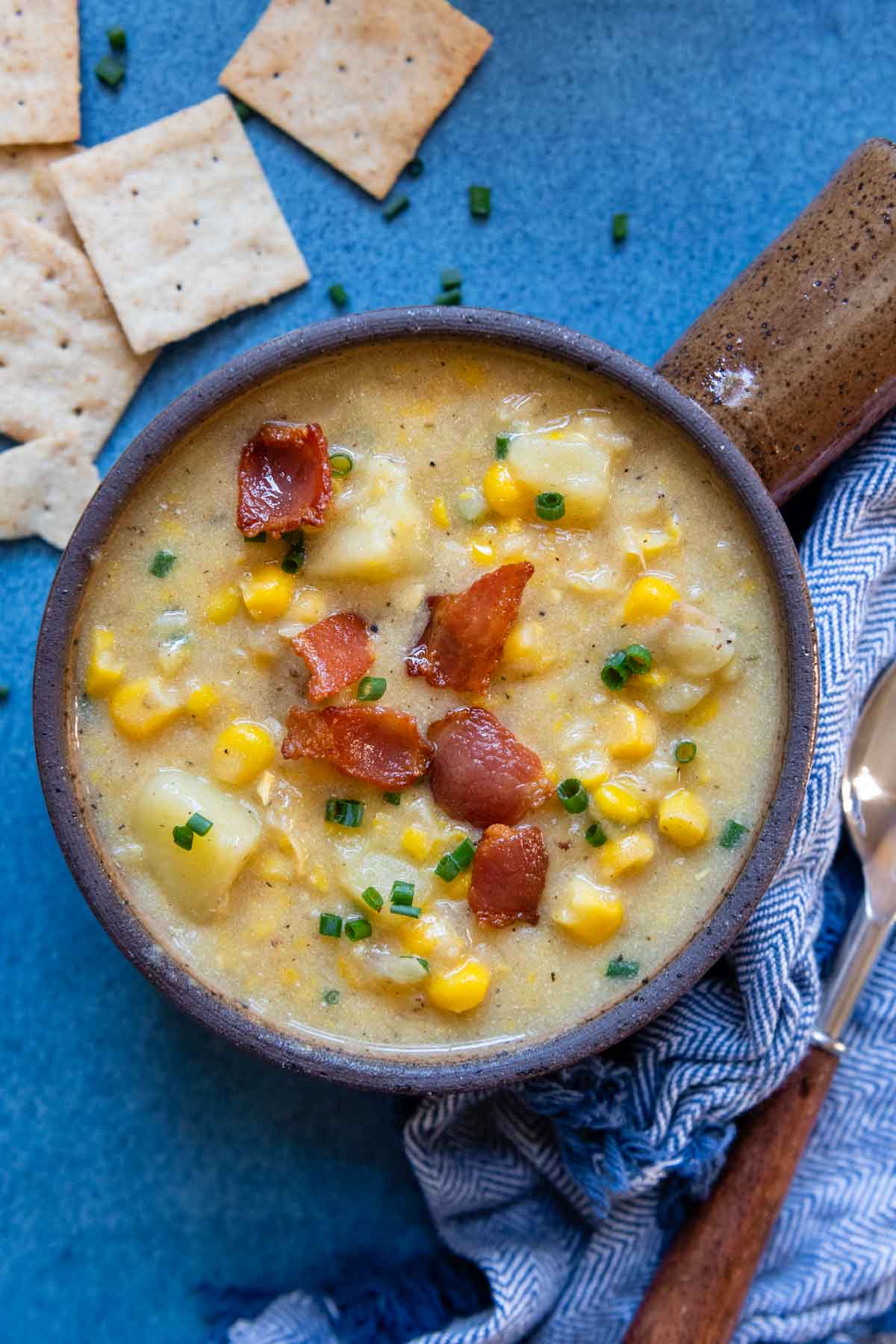 overhead shot of corn chowder with crackers and chives scattered around.