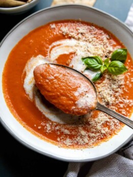 a spoon lifting out of a bowl of tomato soup.
