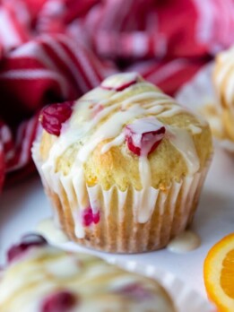 a whole cranberry muffin with glaze on top resting on a white marble surface.
