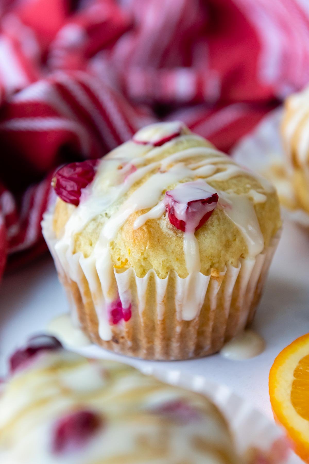 a whole cranberry muffin with glaze on top resting on a white marble surface.