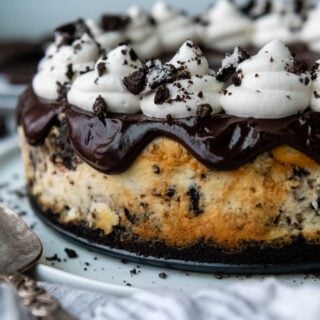 an uncut gluten free oreo cheesecake with ganache and whipped cream on top.