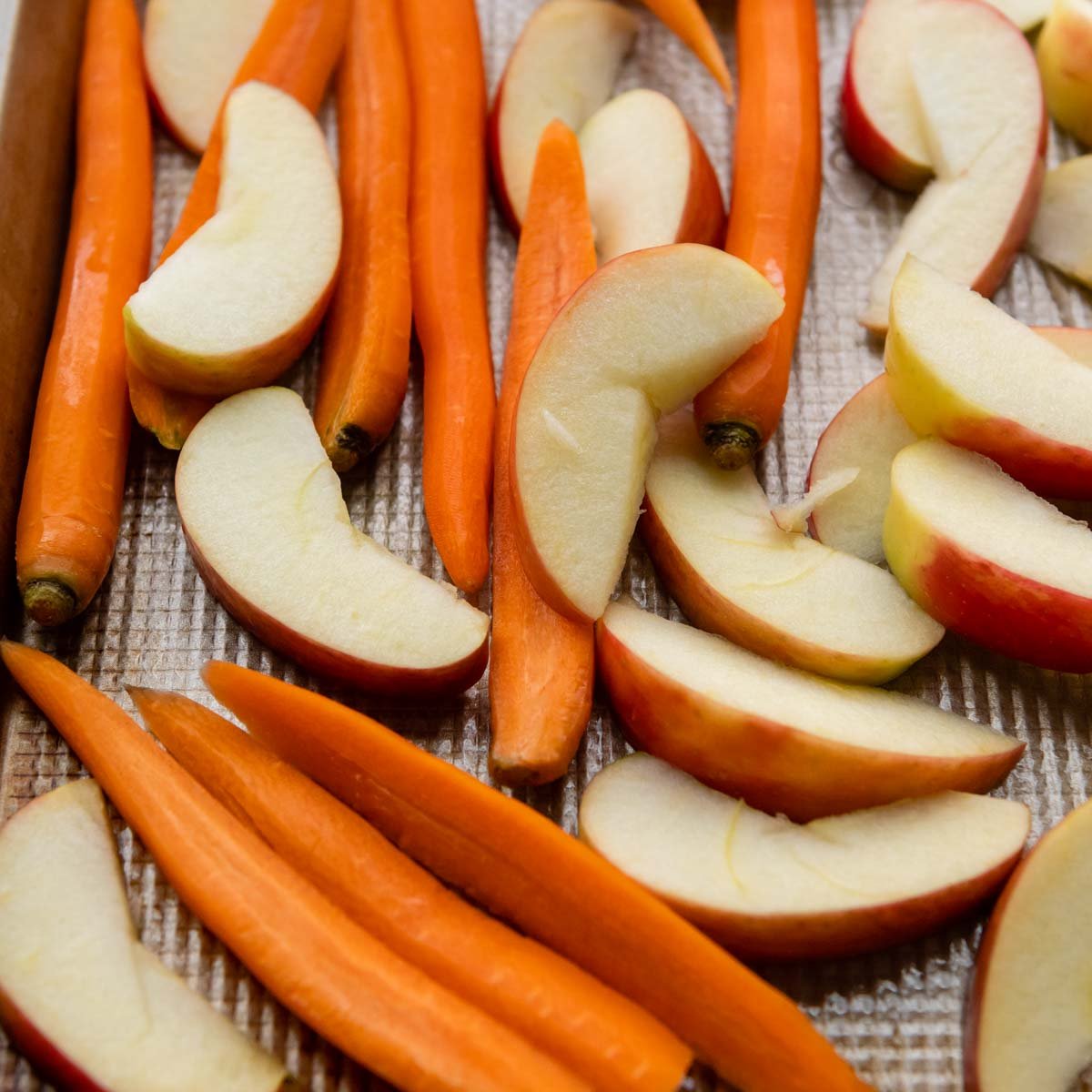 cut, unbaked carrots and apples on a baking pan.