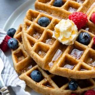 overhead show of oat flour waffles with fresh berries, syrup and butter.