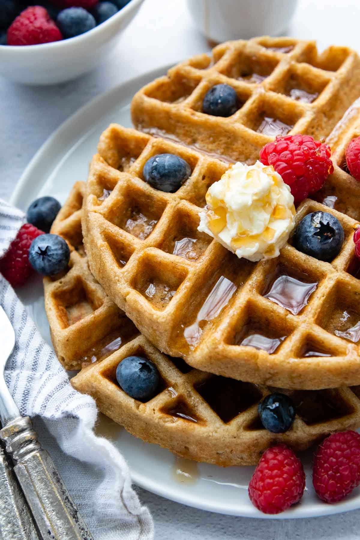 overhead show of oat flour waffles with fresh berries, syrup and butter.