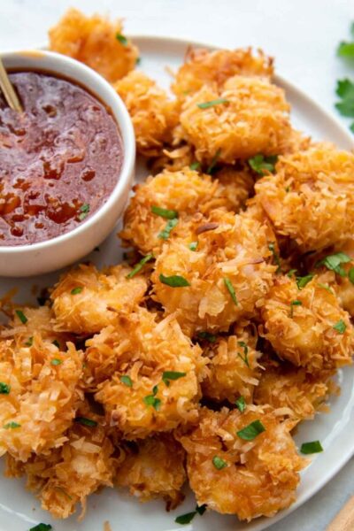 a plate of gluten-free coconut shrimp with a dipping sauce next to it.