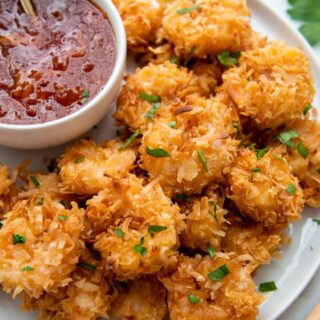 a plate of gluten-free coconut shrimp with a dipping sauce next to it.