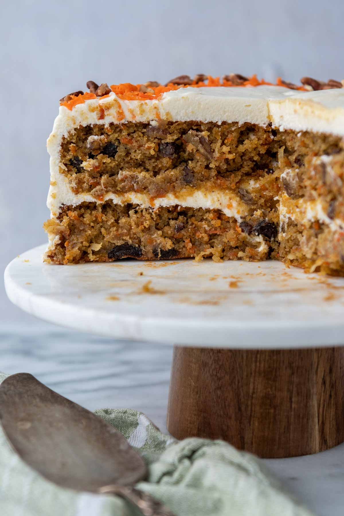 layered carrot cake on a cake stand with a large slice missing.