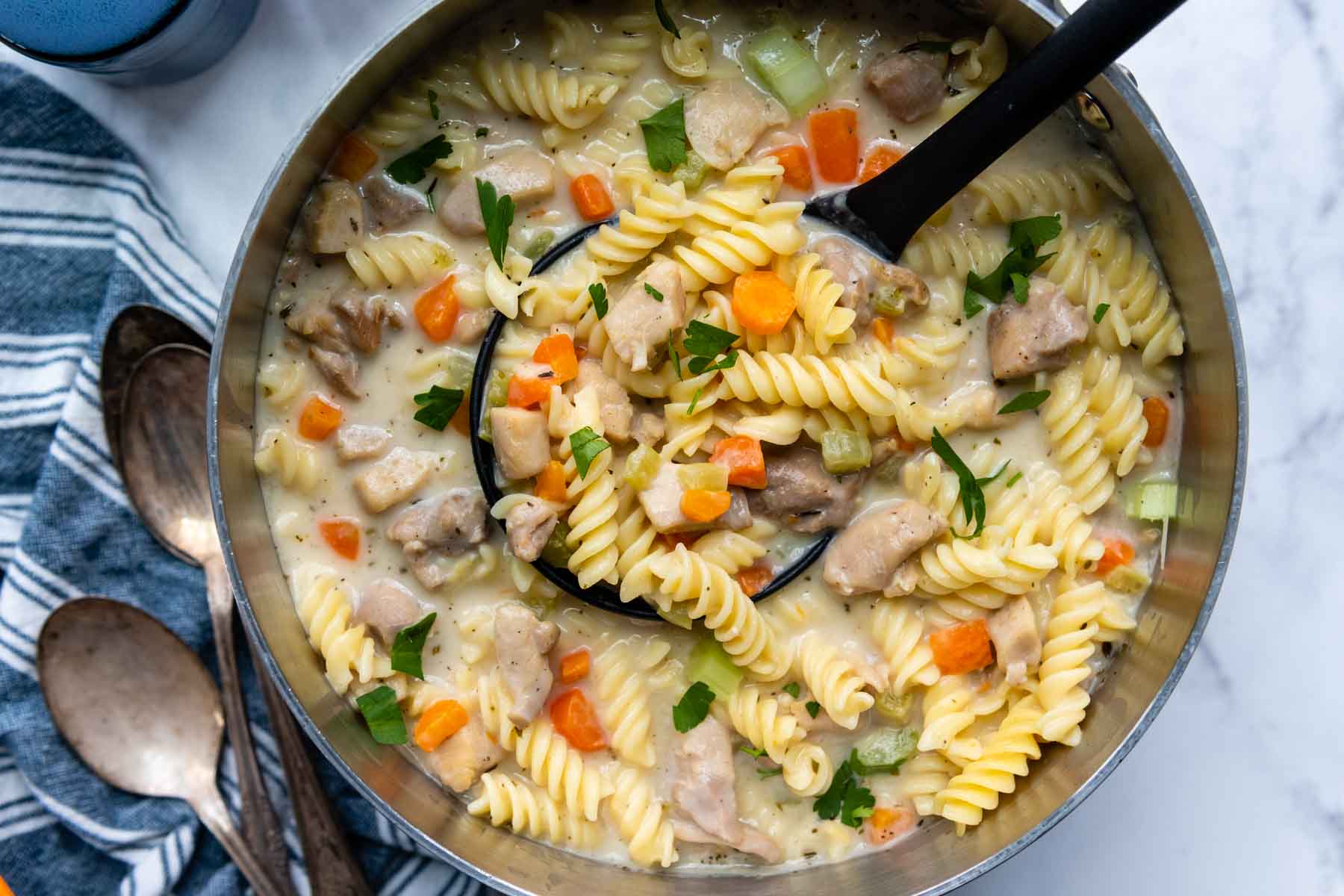 a pot of gluten-free chicken noodle soup with a ladle.