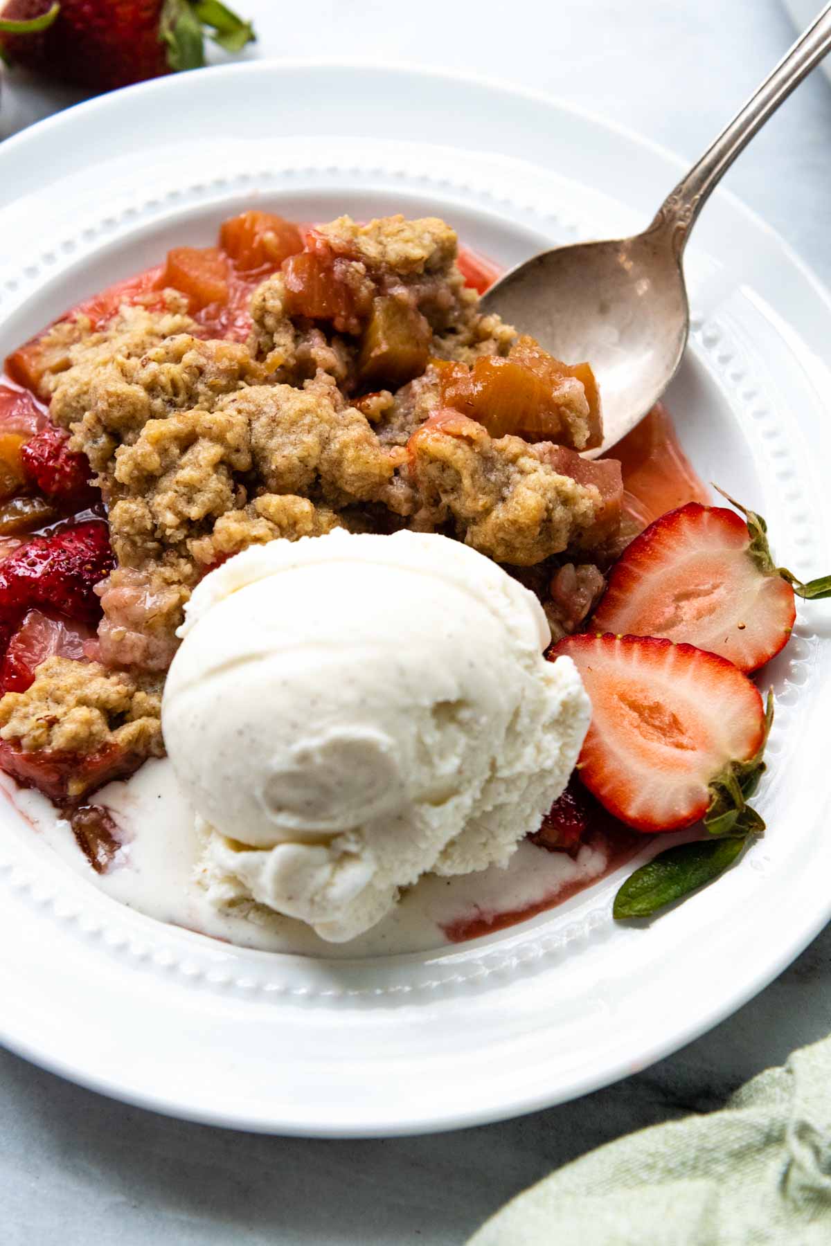 rhubarb crisp on a white plate with ice cream.