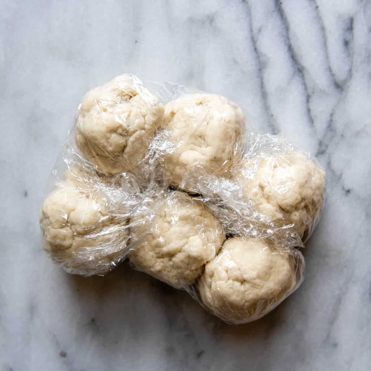 6 balls of dough in plastic wrap.