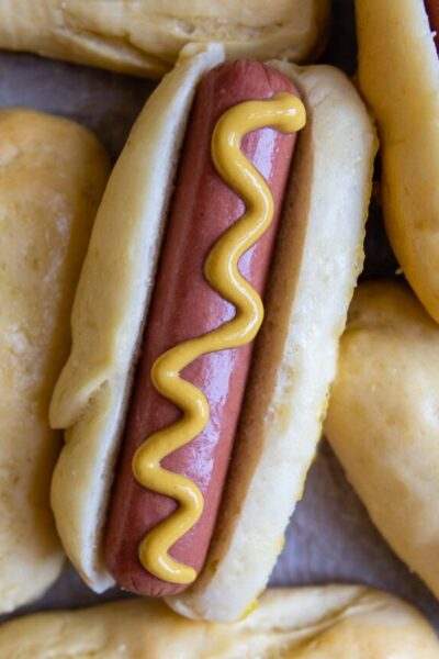 a hot dog with mustard on it resting next to other buns.