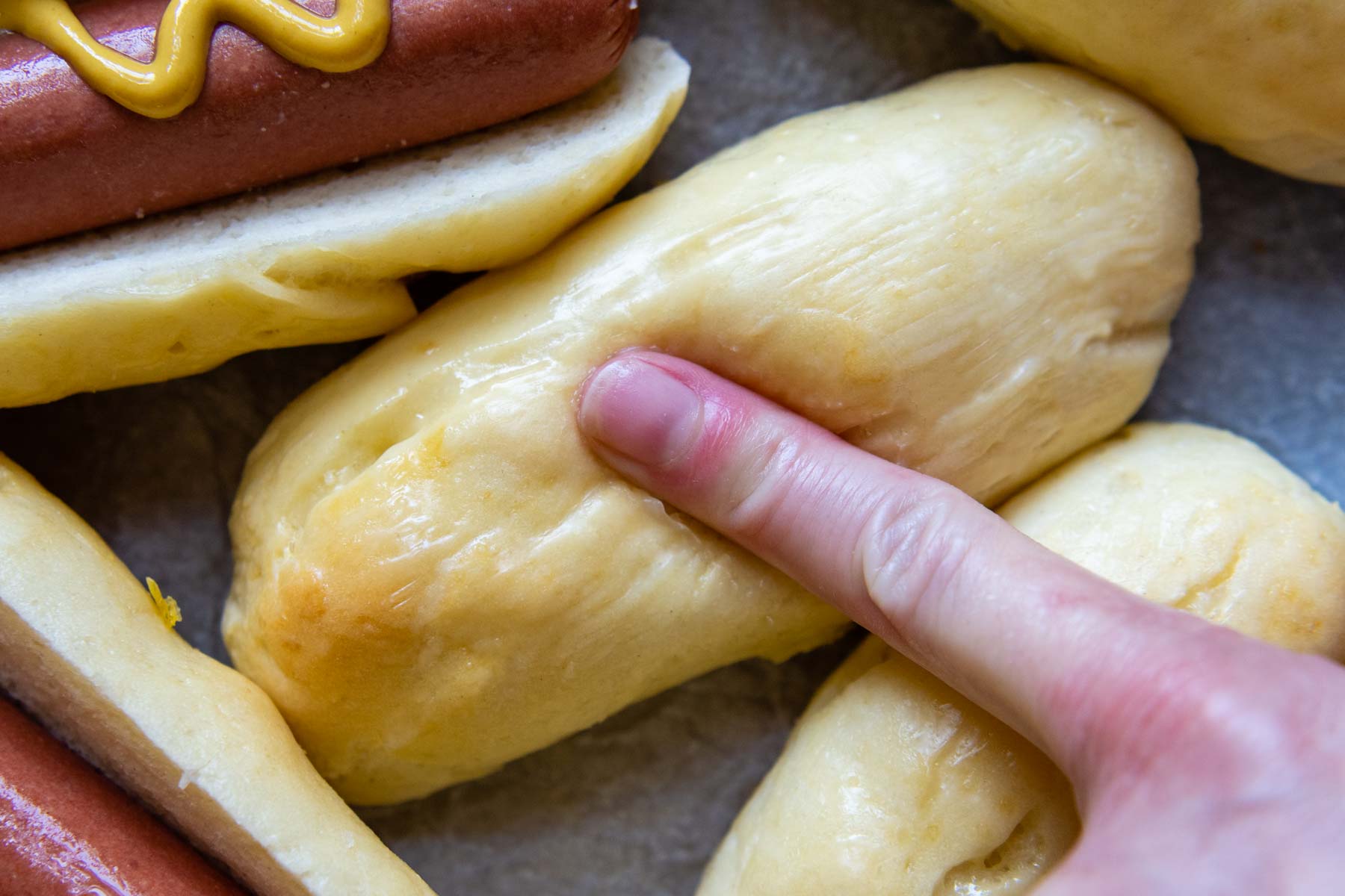 a finger pressing down on a hot dog bun.