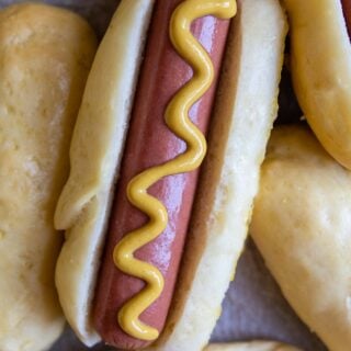 a hot dog with mustard on it resting next to other buns.