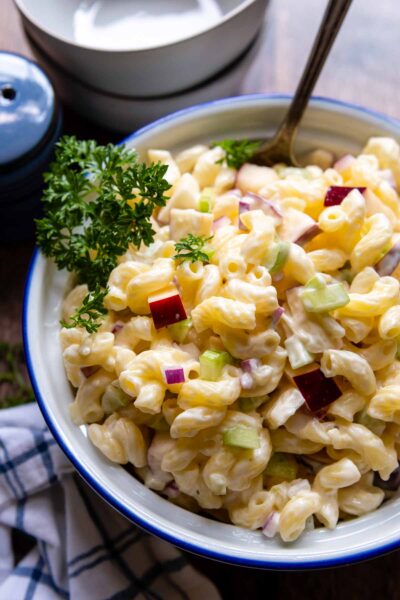 a spoon going into a bowl of macaroni salad with parsley garnish on top.