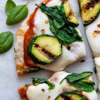 close up of a slice of grilled pizza with basil leaves next to it.