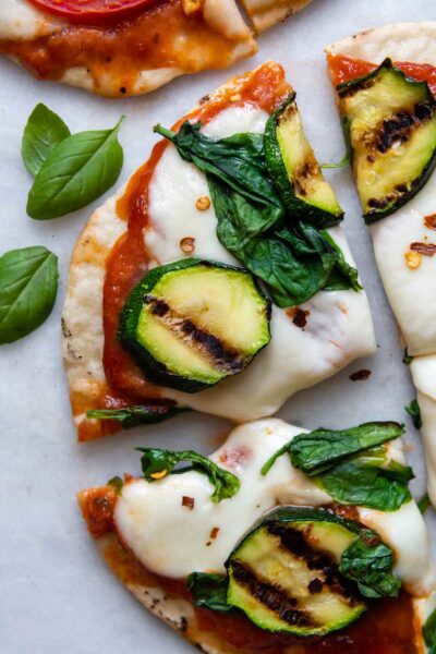 close up of a slice of grilled pizza with basil leaves next to it.