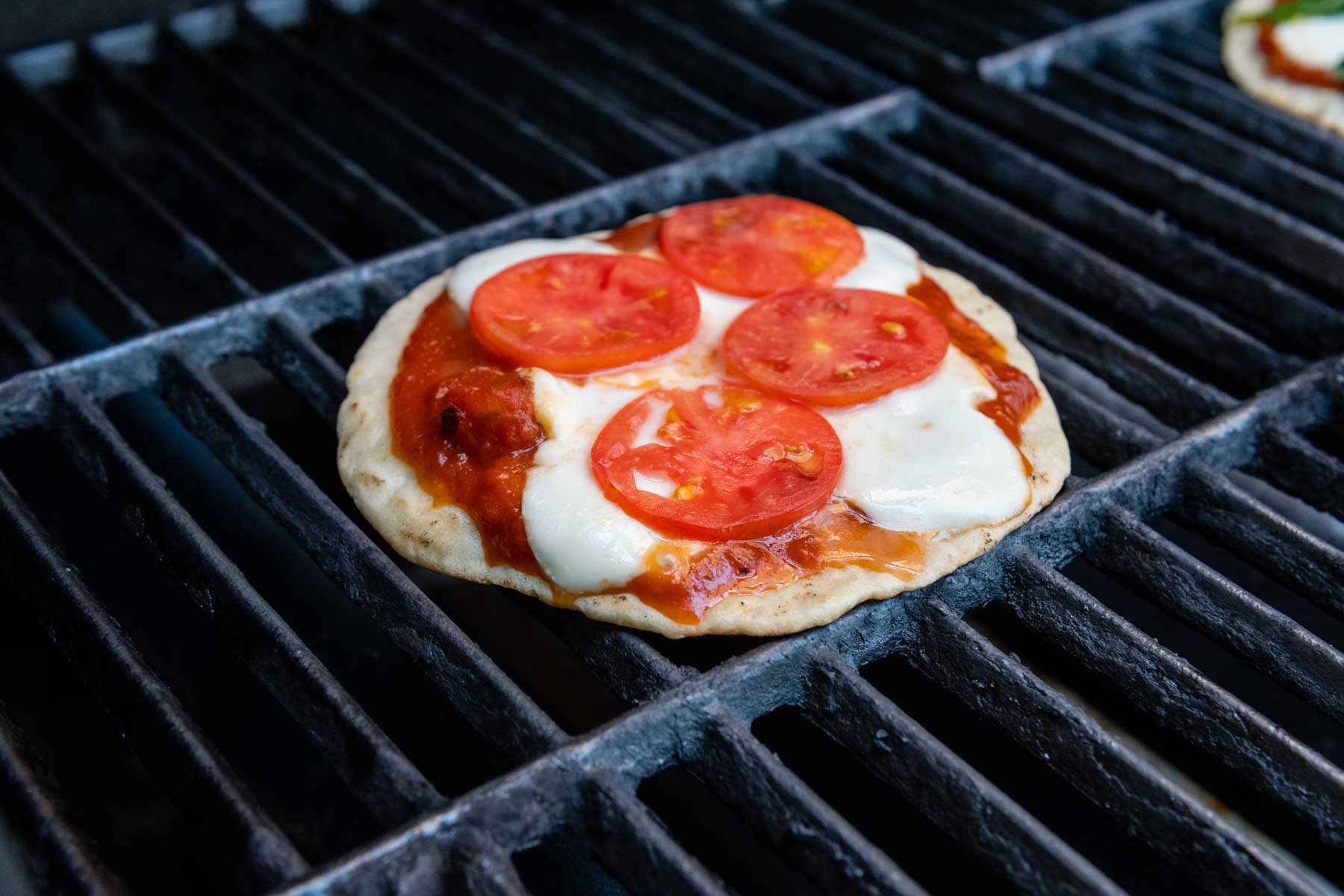 a pizza cooking on a grill with tomatoes and mozzarella.