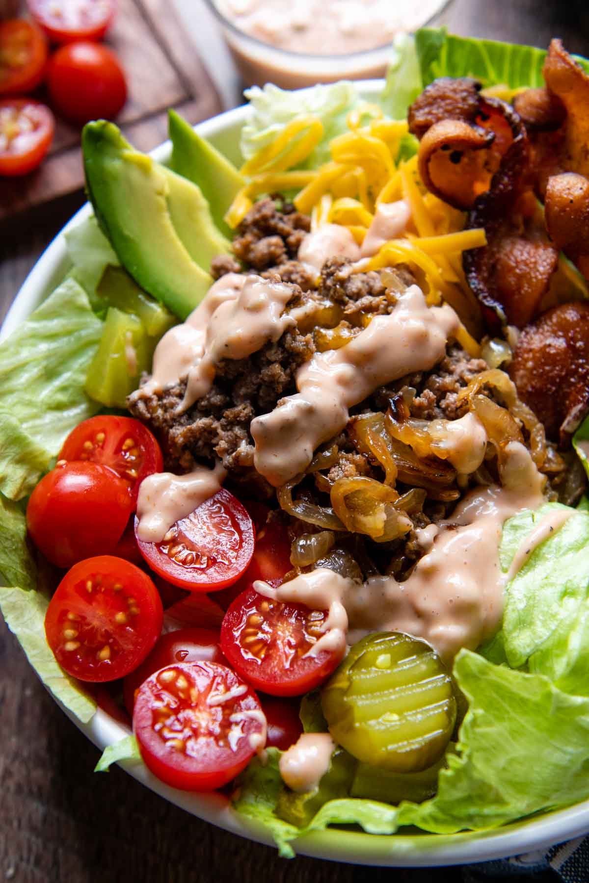 a burger bowl in a white bowl with sauce drizzled on top.