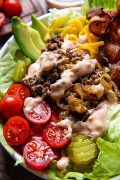 a burger bowl in a white bowl with sauce drizzled on top.