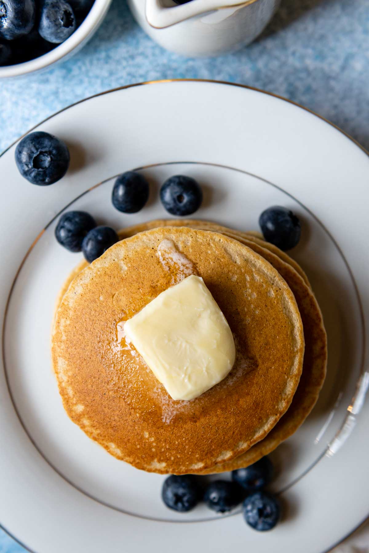 stack of pancakes on a white plate with blueberries scattered around.