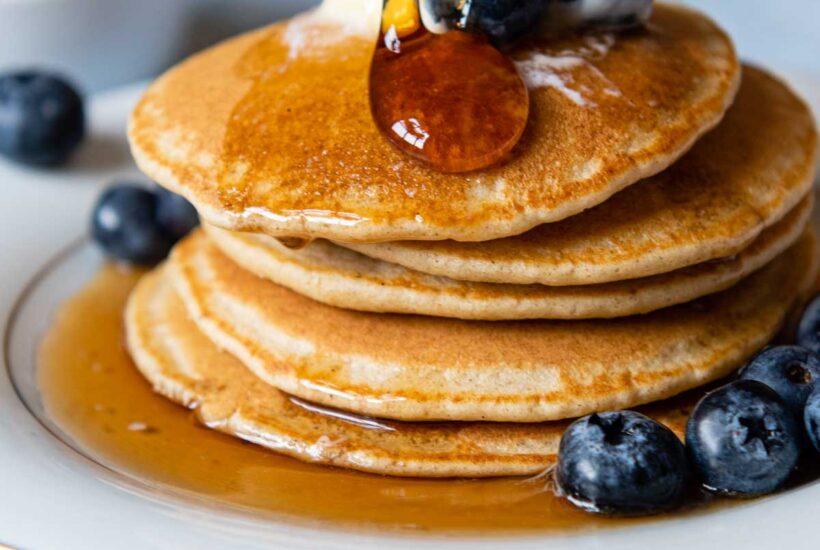 syrup being poured on a stack of pancakes.