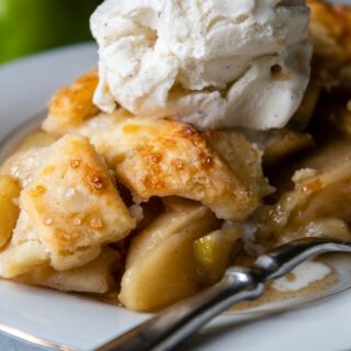a slice of apple pie on a white plate with ice cream on top.